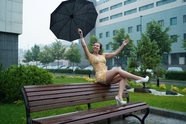 阴雨天坐在公共长椅上撑伞的美女图片